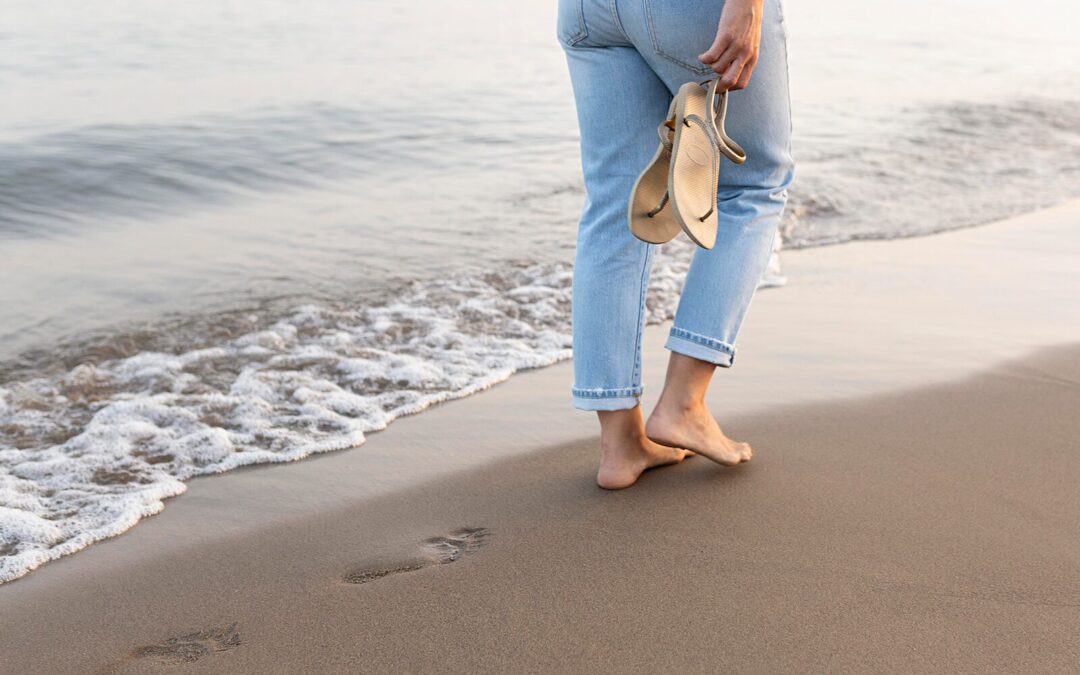 Person walking barefoot along the shoreline holding sandals