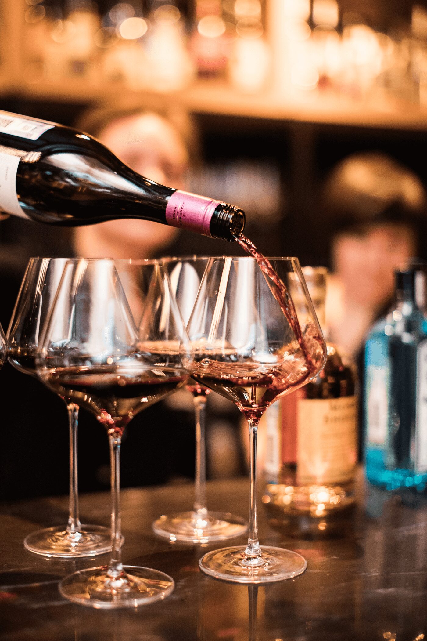 Red wine being poured into glasses at a busy bar