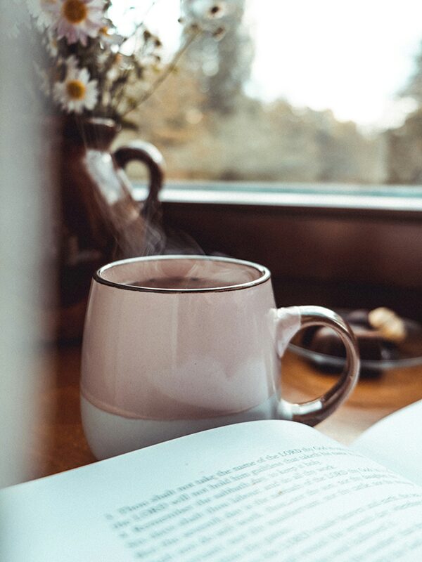 Mug of steaming tea with book in front of a window